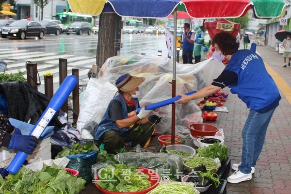 바르게살기운동 광주광역시 광산구협의회 이선미 여성회장이 너무 땀이 많이 나 아예 우의를 벗고 태극기를 나눠주고 있다.