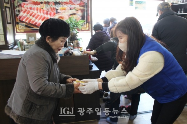 운남동 바르게살기위원회 엄기숙 여성회장이 어르신들이 떡국 점심을 마치고 나가시는 길 출구에서 식혜와 유과를 일일이 손에 쥐어드리고 있다.