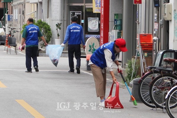 월곡1동 바르게살기위원회 김소영 여성위원장이 집에서 빗자루와 쓰레받기를 가져와 골목길 쓰레기를 쓸어담고 있다. 앞쪽에 유관수 위원과 서선웅 위원이 봉투를 함께 잡고 줍깅을 하고 있다.